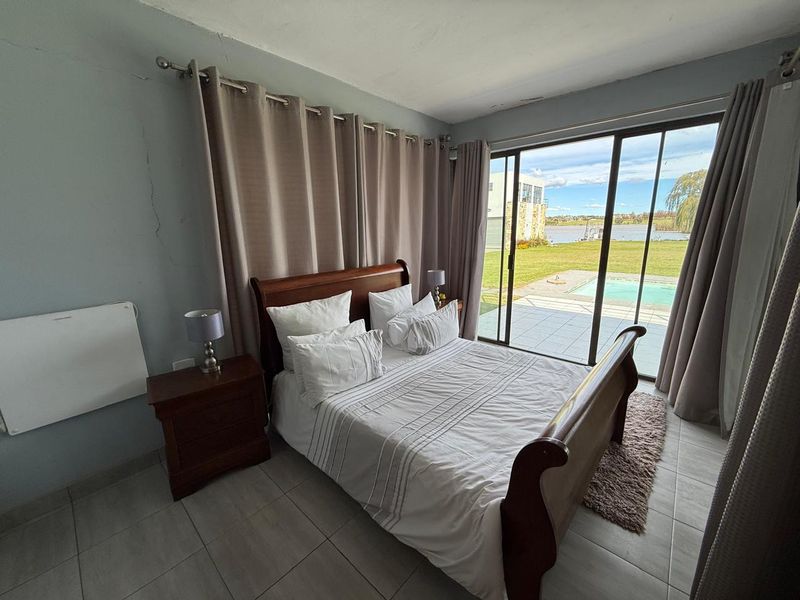 Bedroom featuring tiled flooring and large sliding glass doors providing direct access to the patio and pool area with scenic water views.