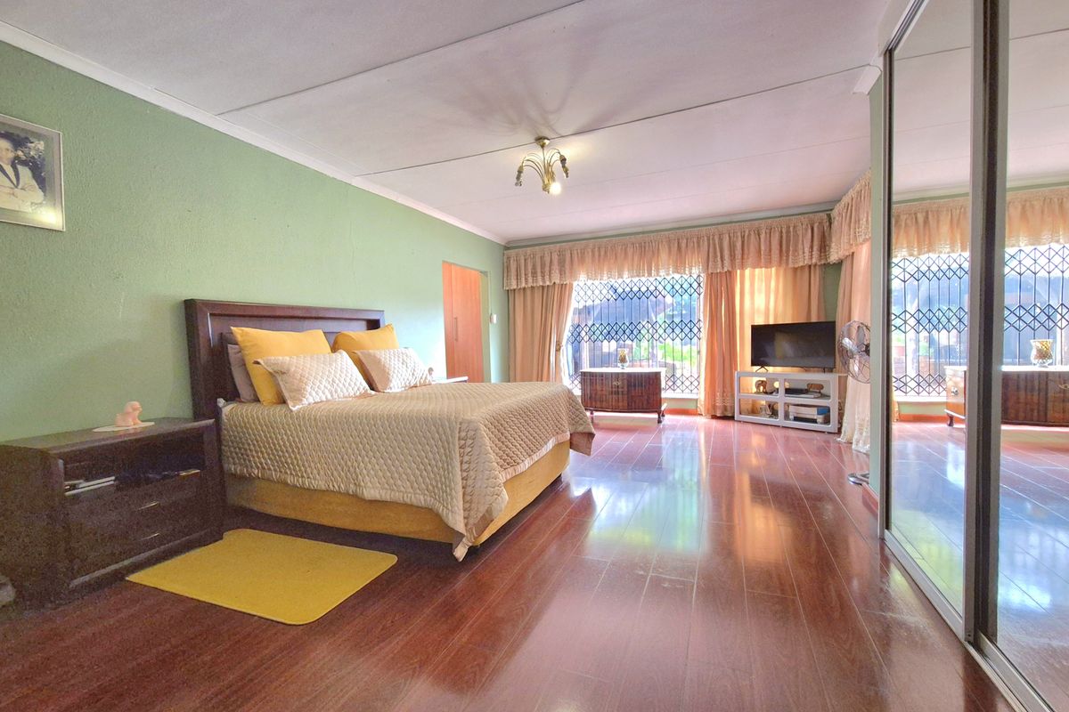 Spacious bedroom featuring polished wooden flooring, large mirrored built-in cupboards, and security gates on the windows.