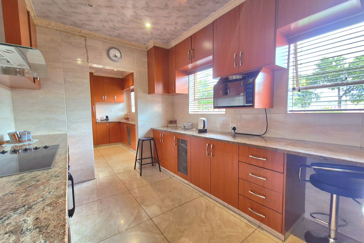 Spacious kitchen featuring wood-finish cabinetry, granite countertops, integrated oven, and tiled flooring, with an adjoining scullery area for additional prep and storage space.