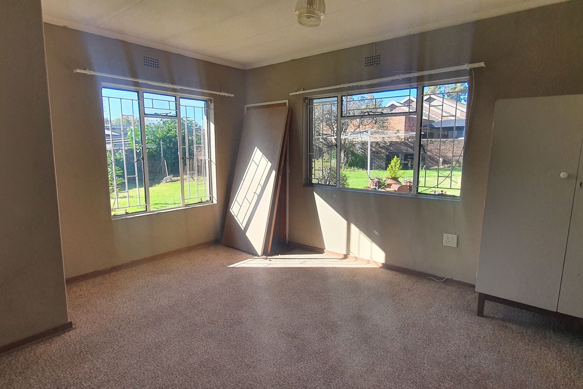 A spacious bedroom featuring large windows with security bars, carpeted flooring, and neutral wall tones, offering a blank canvas for potential updates.