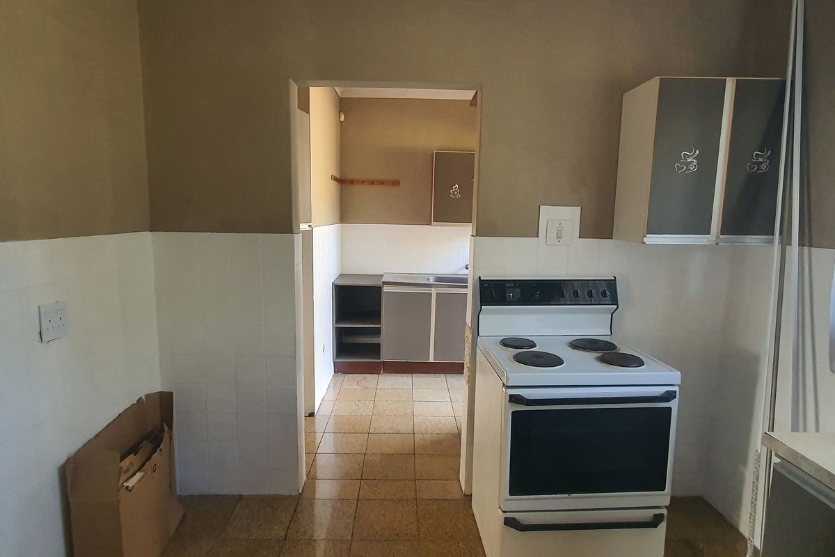 A functional kitchen area featuring tiled splashbacks, built-in cabinetry, and a freestanding electric stove, with an adjacent scullery or prep area visible through the doorway.