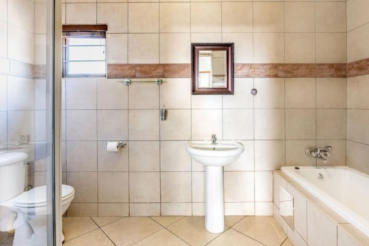 A functional bathroom featuring a pedestal basin, a built-in bathtub with tiled surround, and a separate glass-enclosed shower unit.