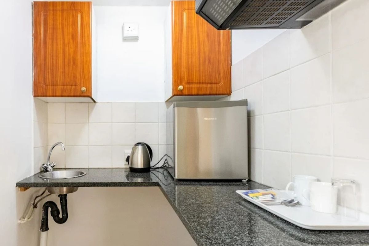 Compact kitchenette area featuring granite countertops, wall-mounted wooden cabinetry, a stainless steel sink, and a built-in extractor fan.