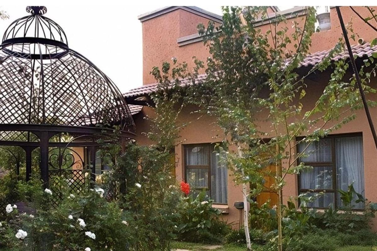 A view of the guest house exterior featuring a landscaped garden, mature trees, and a decorative metal gazebo structure.