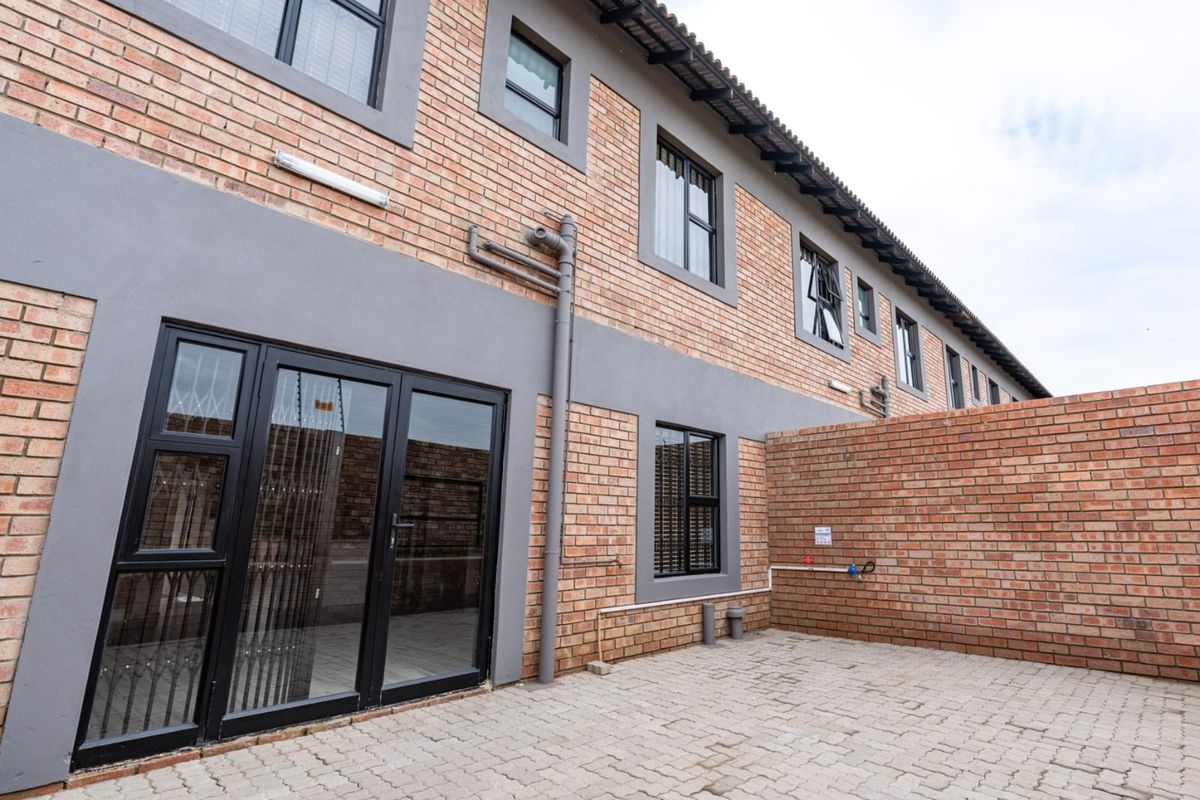 Rear view of the townhouse featuring a paved courtyard, brick facade, and black-framed glass sliding doors leading into the interior.