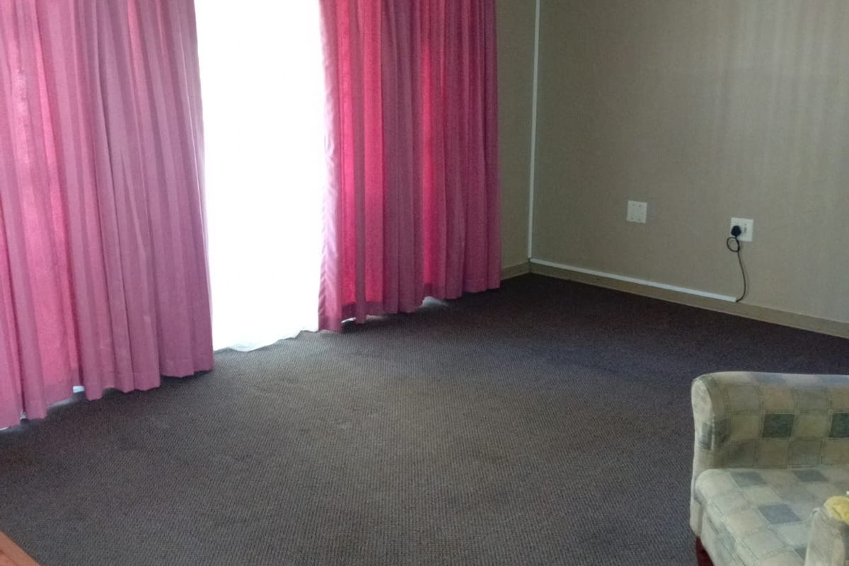 A living room area featuring carpeted flooring, a ceiling fan, and a curtain pelmet, offering a blank canvas for potential interior updates.
