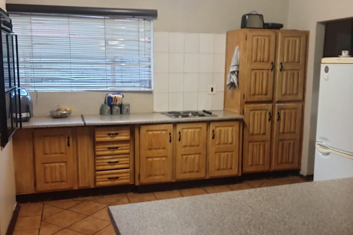 A functional kitchen featuring wooden cabinetry, a built-in hob, tiled flooring, and a breakfast counter, offering a classic layout with ample storage space.