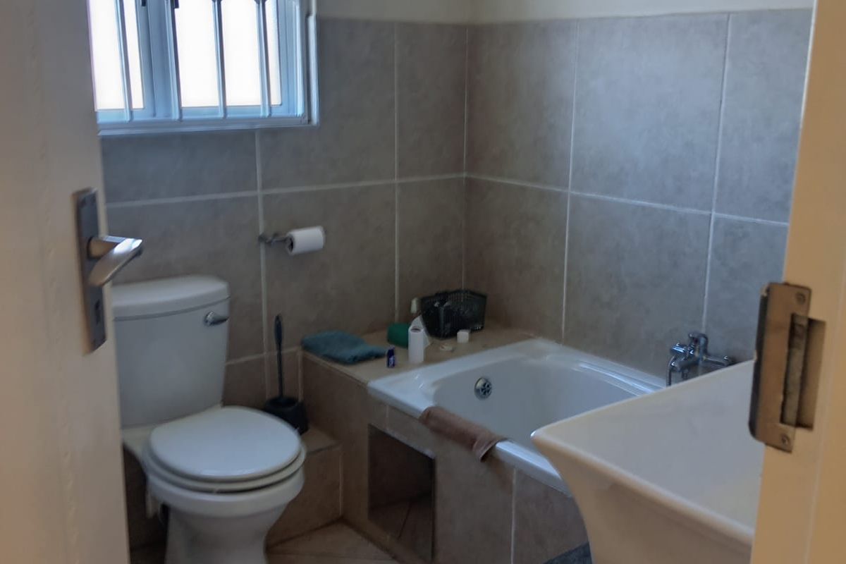 A functional bathroom featuring a built-in bathtub, toilet, and vanity basin with neutral wall and floor tiling.