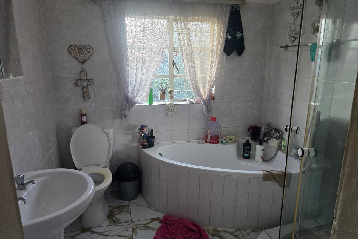 A functional bathroom featuring a corner bathtub, separate glass shower enclosure, pedestal basin, and tiled finishes throughout.