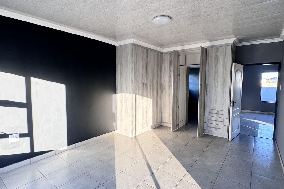 A spacious, empty bedroom featuring modern built-in cupboards, neutral tiled flooring, and a textured ceiling finish with a dark accent wall.