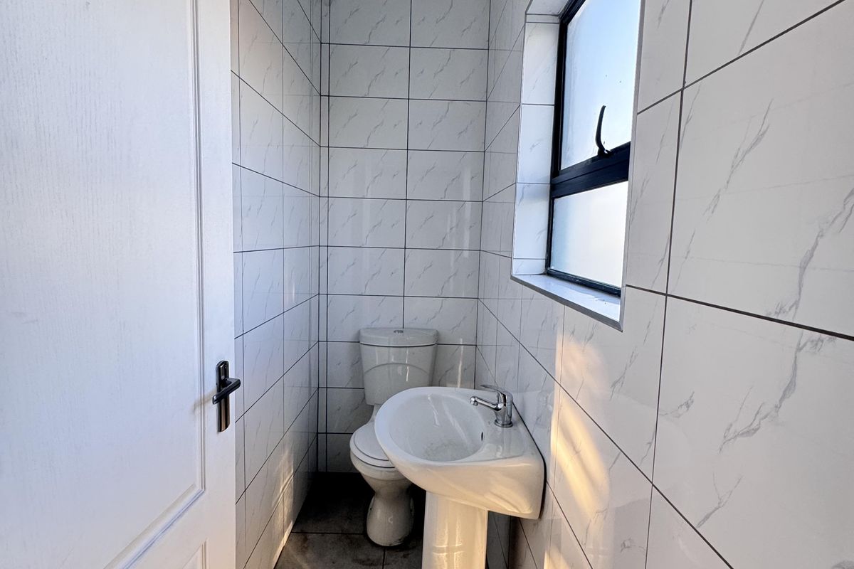 A compact, modern bathroom featuring floor-to-ceiling marble-look wall tiles, a pedestal basin, and a standard toilet.