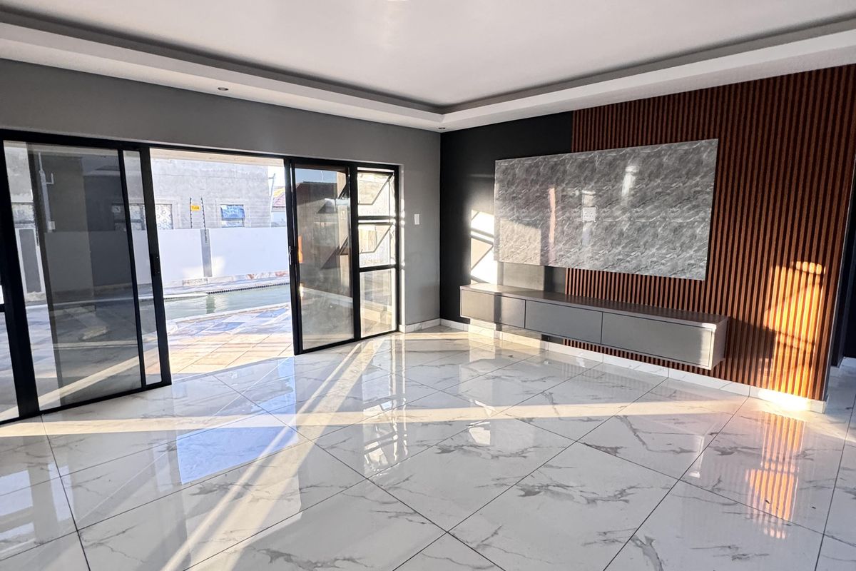 Modern living room featuring large-format porcelain tiles, a stylish slat wood feature wall with built-in media console, and seamless access to the outdoor area.
