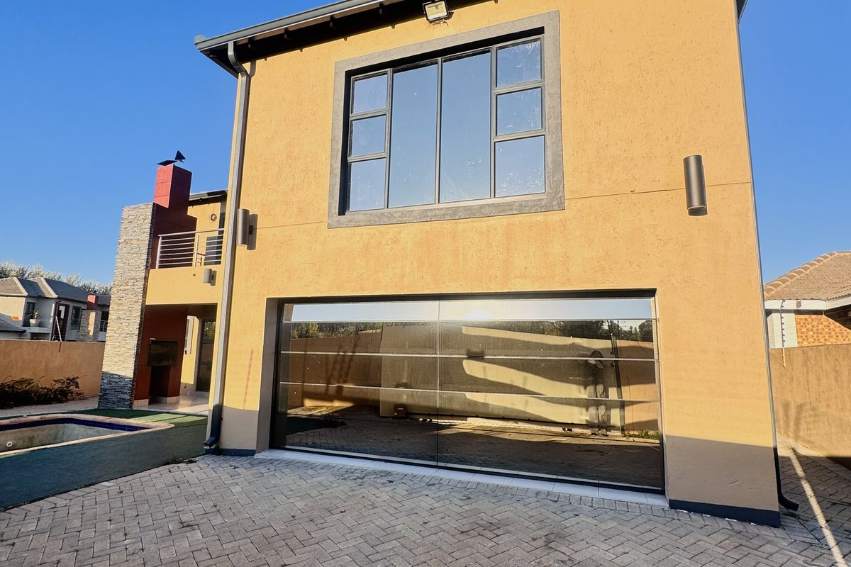 Rear view of the property featuring a modern garage door, paved driveway, swimming pool, and stone-clad balcony area.