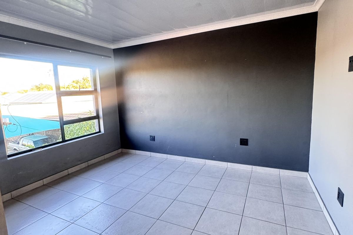 A vacant bedroom featuring neutral tiled flooring, a dark accent wall, and an aluminium-framed window providing natural light.