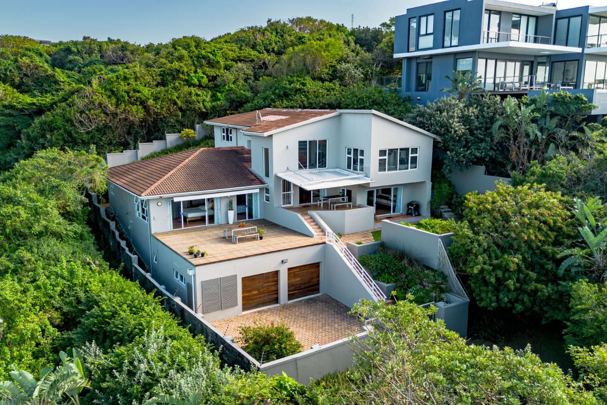 Aerial view of a multi-level residential property featuring a double garage, paved driveway, expansive timber decking, and tiered outdoor living spaces.