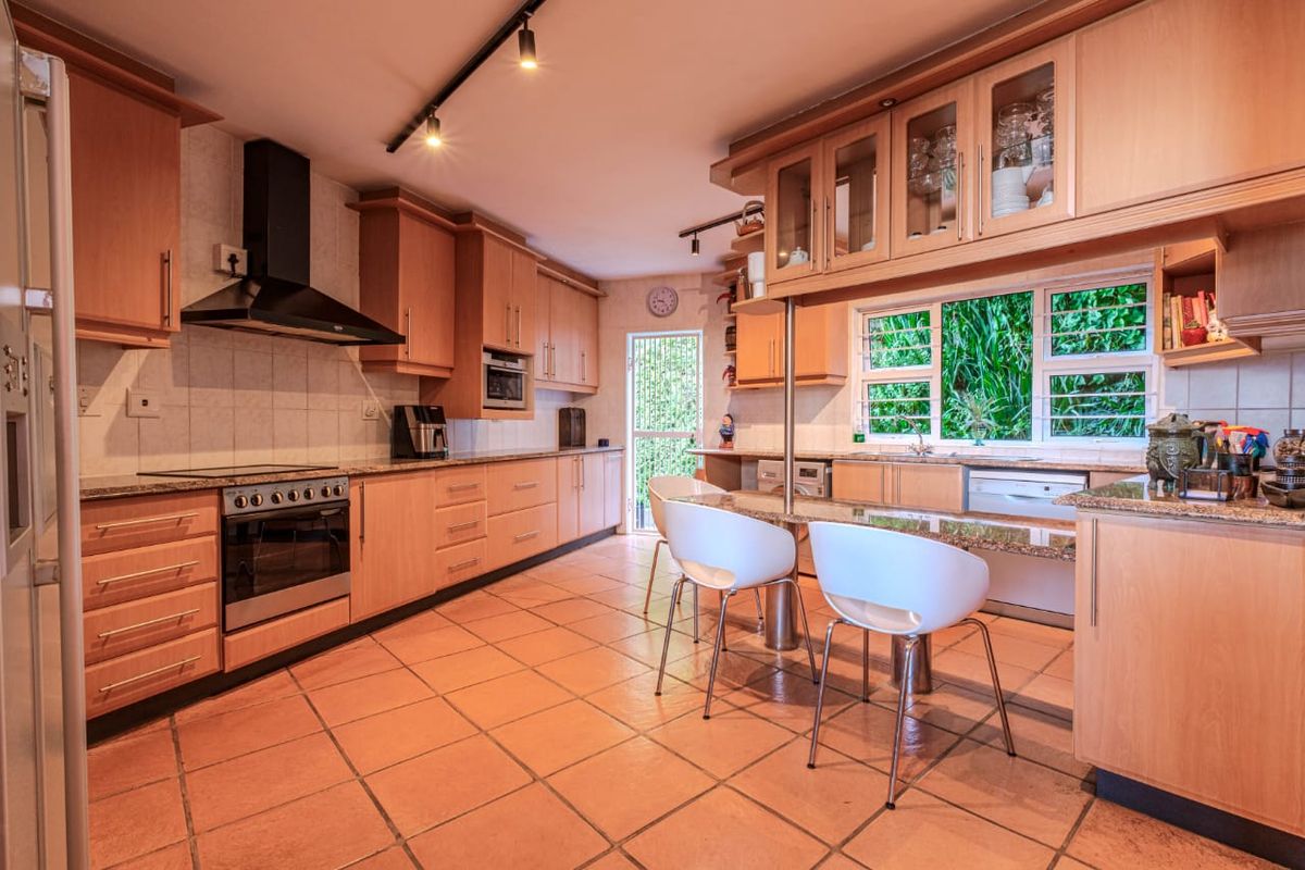 Spacious kitchen featuring light wood cabinetry, granite countertops, integrated appliances, and a breakfast bar, with direct access to the garden.