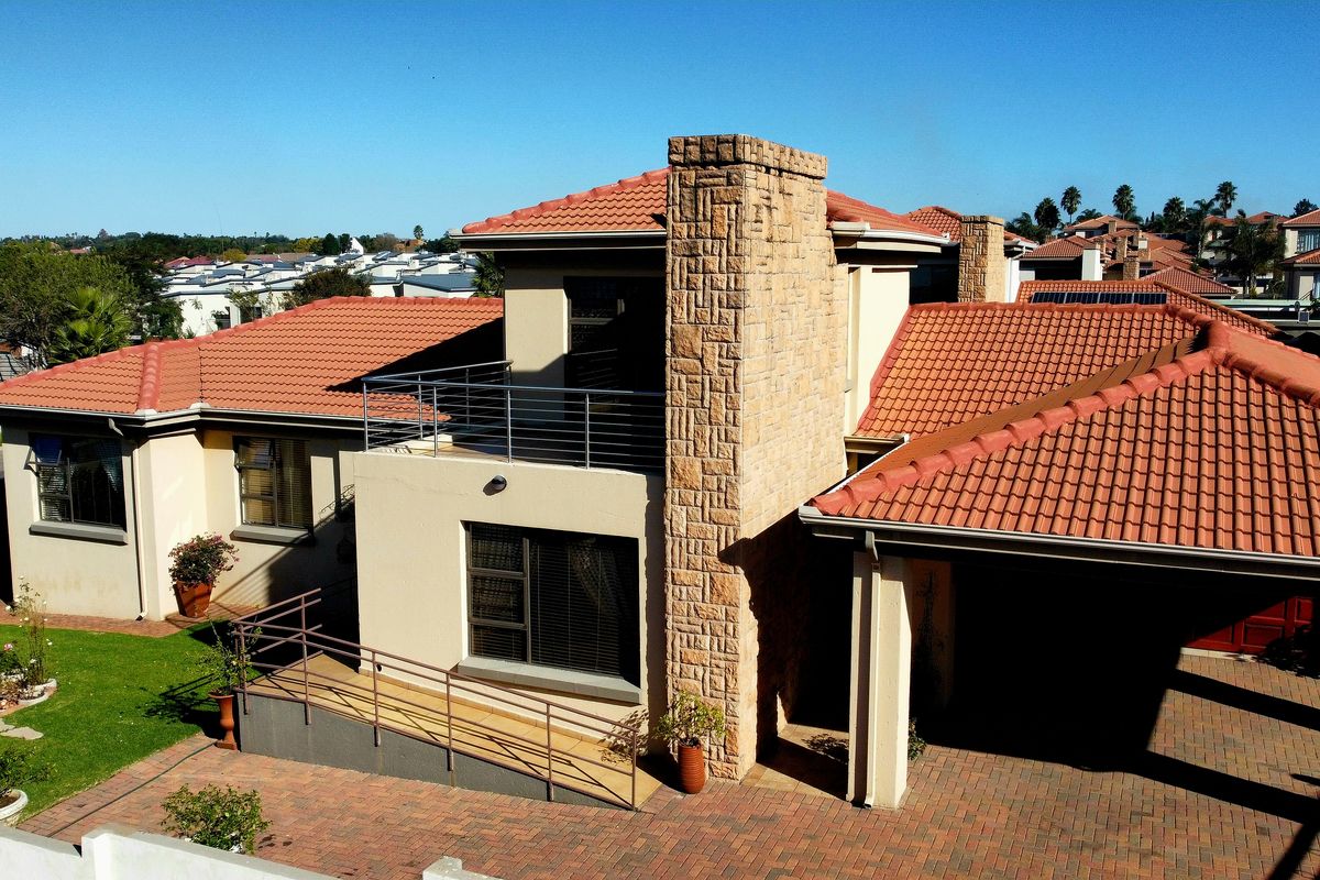 Aerial view of the rear exterior featuring a terracotta tiled roof, stone-clad chimney, balcony, paved driveway, and a wheelchair-accessible ramp.