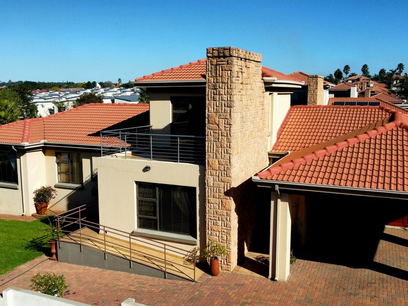 Aerial view of the rear exterior featuring a terracotta tiled roof, stone-clad chimney, balcony, paved driveway, and a wheelchair-accessible ramp.