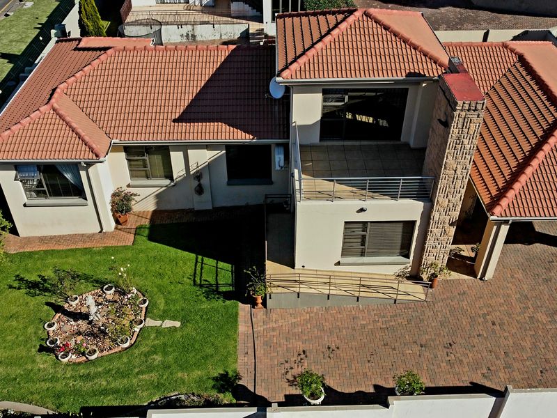 Aerial view of a residential property featuring a tiled roof, stone chimney, paved driveway, and a well-maintained garden with a balcony.