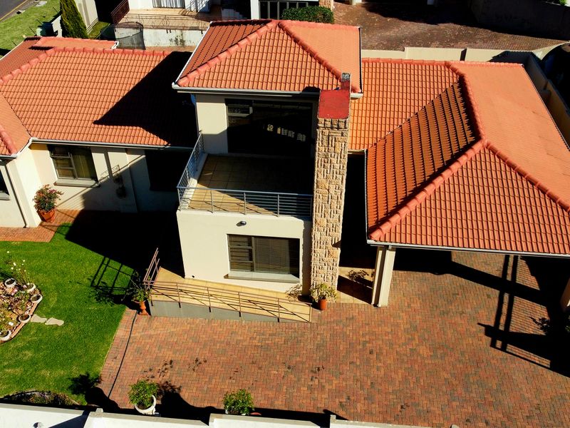 Aerial view of the property showcasing the tiled roof, stone-clad chimney, paved driveway, covered carport, and landscaped garden area.