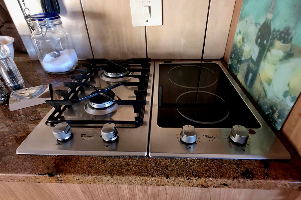 A kitchen workspace featuring a dual-hob setup with both a gas burner and an electric ceramic cooktop integrated into a granite countertop.