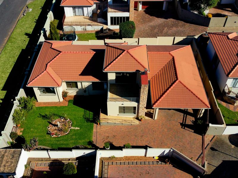 Aerial view of a residential property featuring a tiled roof, paved driveway, and a landscaped garden within a secure boundary wall.