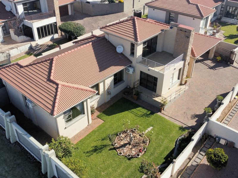 Aerial view of a residential property featuring a tiled roof, paved driveway, balcony, and a private garden area within a secure estate.