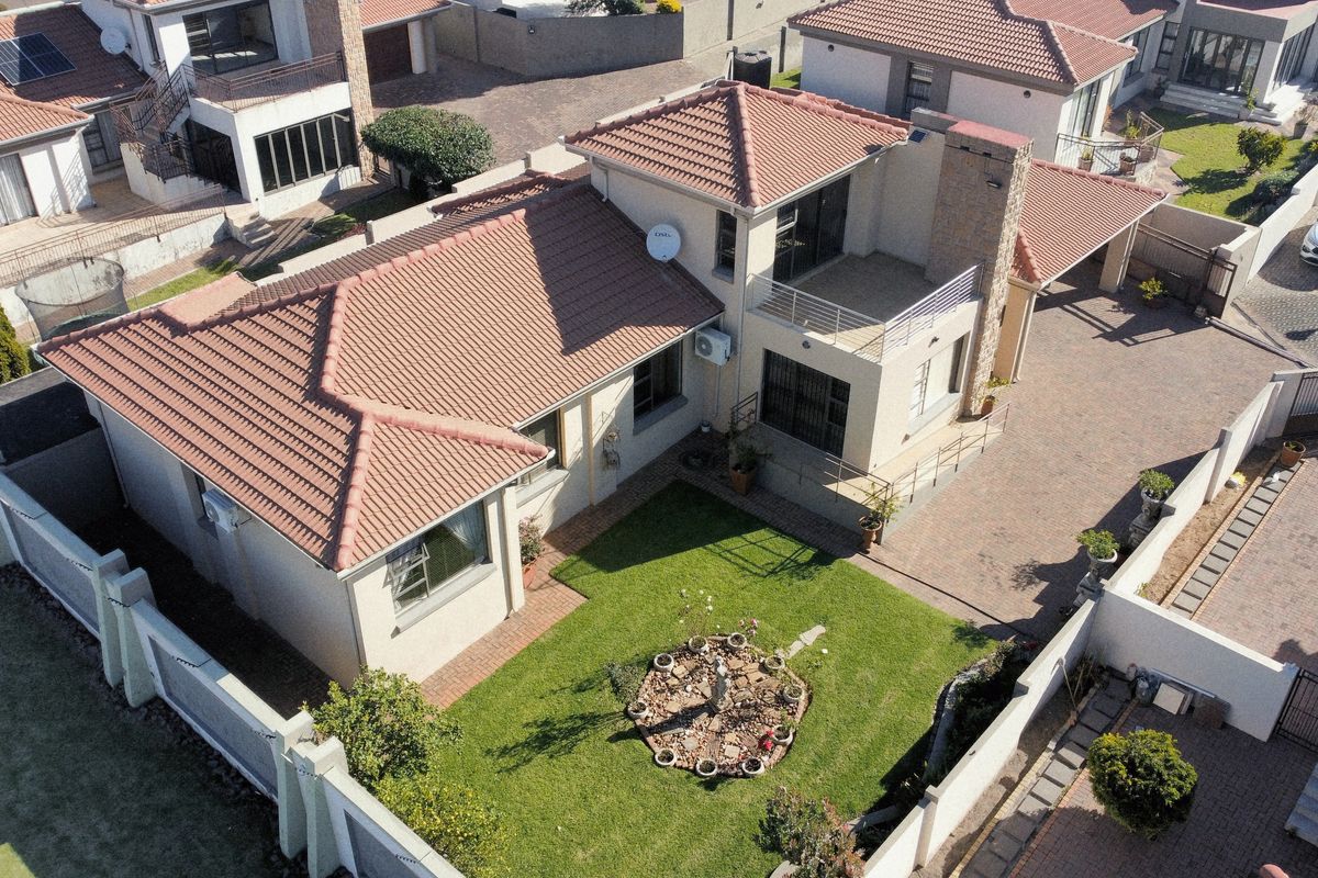 Aerial view of a residential property featuring a tiled roof, paved driveway, balcony, and a private garden area within a secure estate.