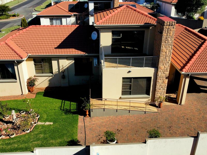 Aerial view of a residential property featuring a terracotta tiled roof, stone chimney, paved driveway, and a balcony with metal railings.