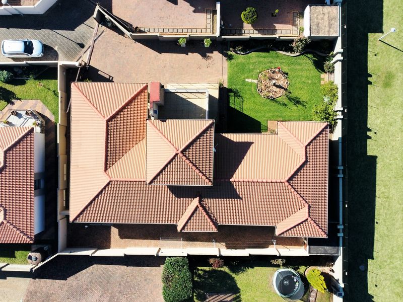 Aerial view of the property showcasing the tiled roof structure, paved driveway, surrounding boundary walls, and landscaped garden area.