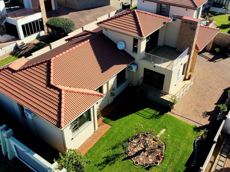 Aerial view of a residential property featuring a terracotta tiled roof, stone chimney, upper-level balcony, and a well-maintained garden with a paved driveway.
