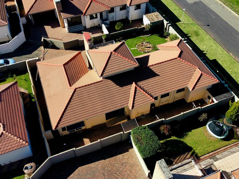 Aerial view of a residential property featuring a tiled roof, paved driveway, and surrounding garden space within a secure boundary wall.