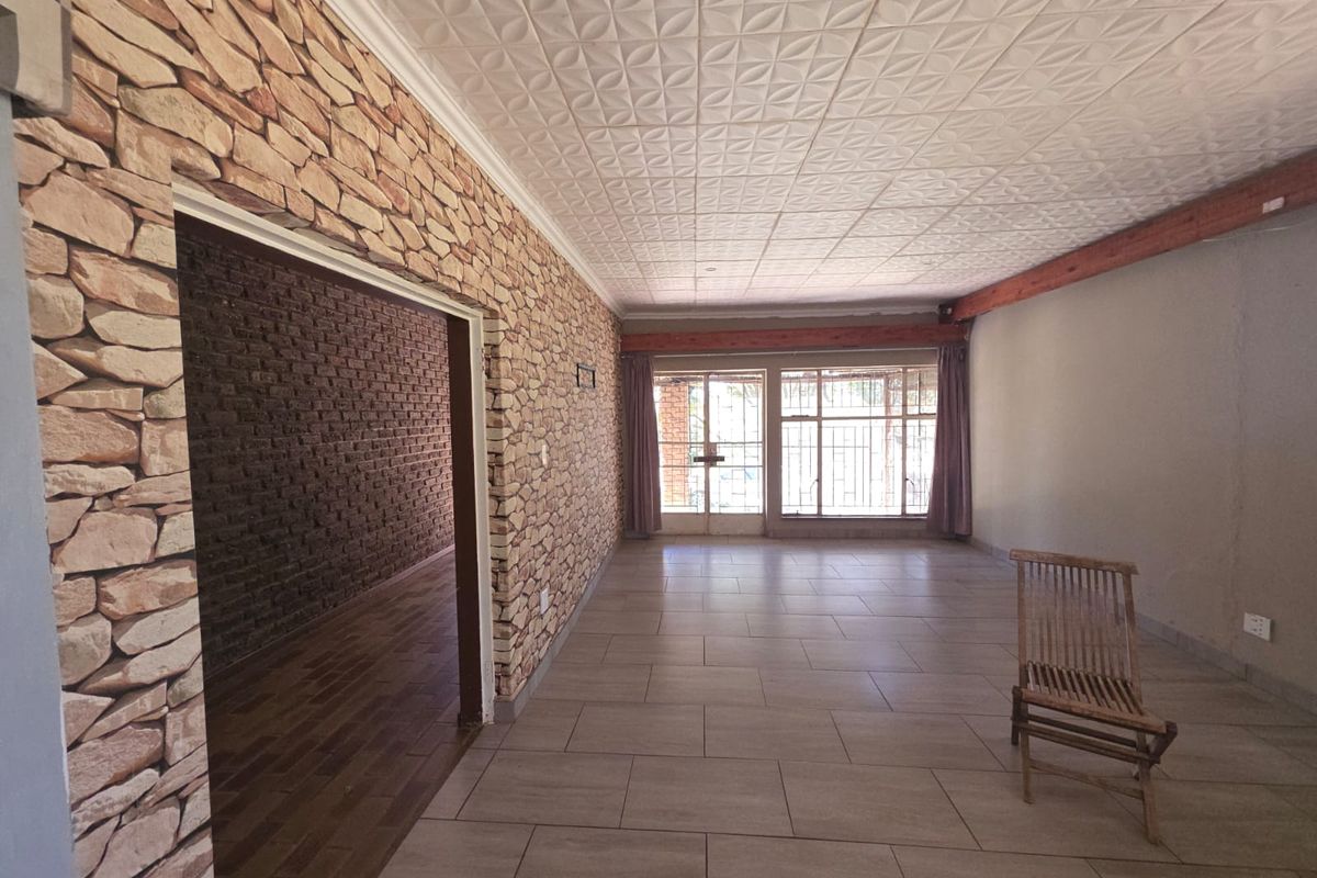 Spacious living area featuring tiled floors, a stone-effect feature wall, and an adjoining room with exposed brickwork, offering a versatile layout.