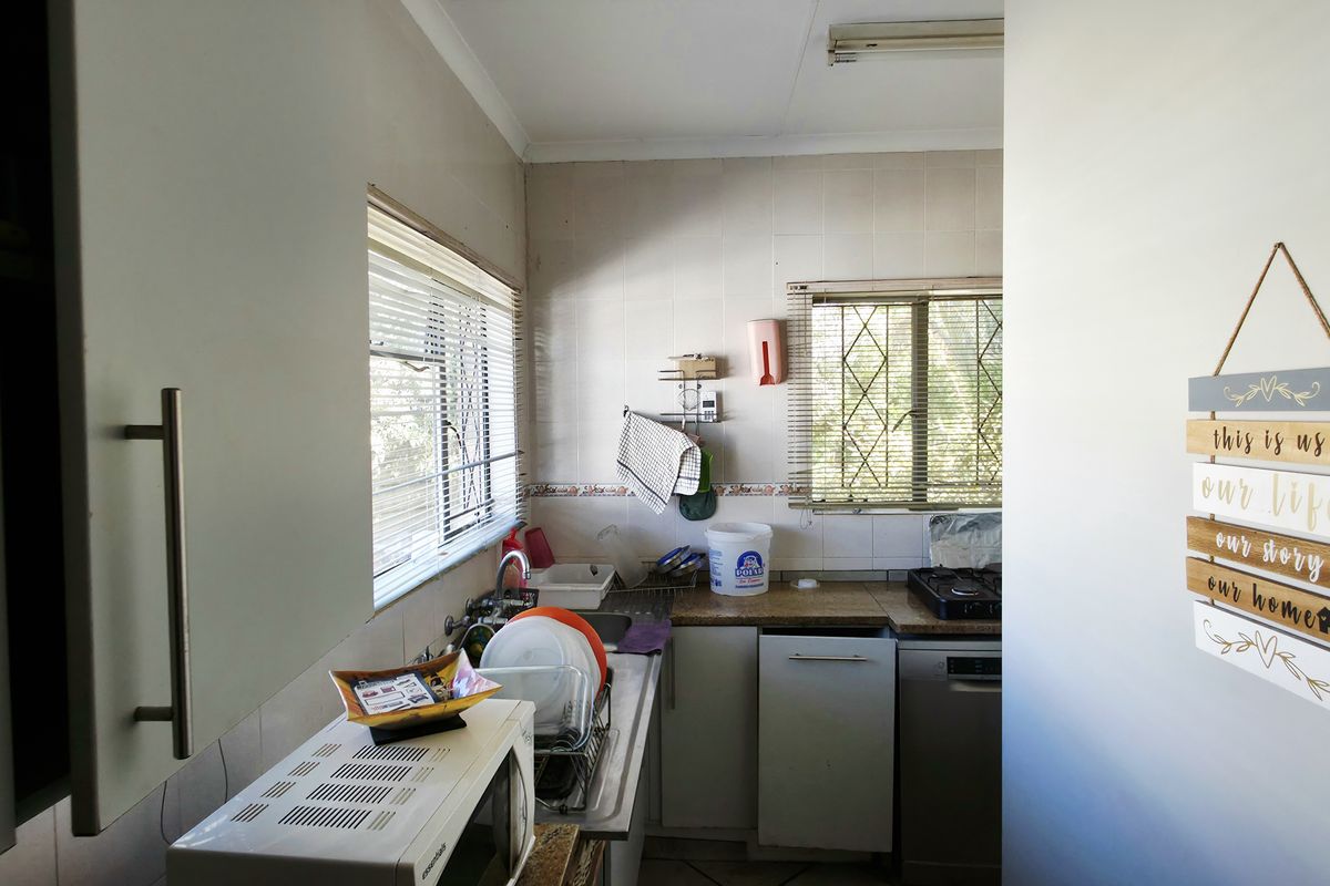 A functional kitchen space featuring built-in cabinetry, tiled splashbacks, and security bars on the windows, offering potential for modernization and cosmetic updates.