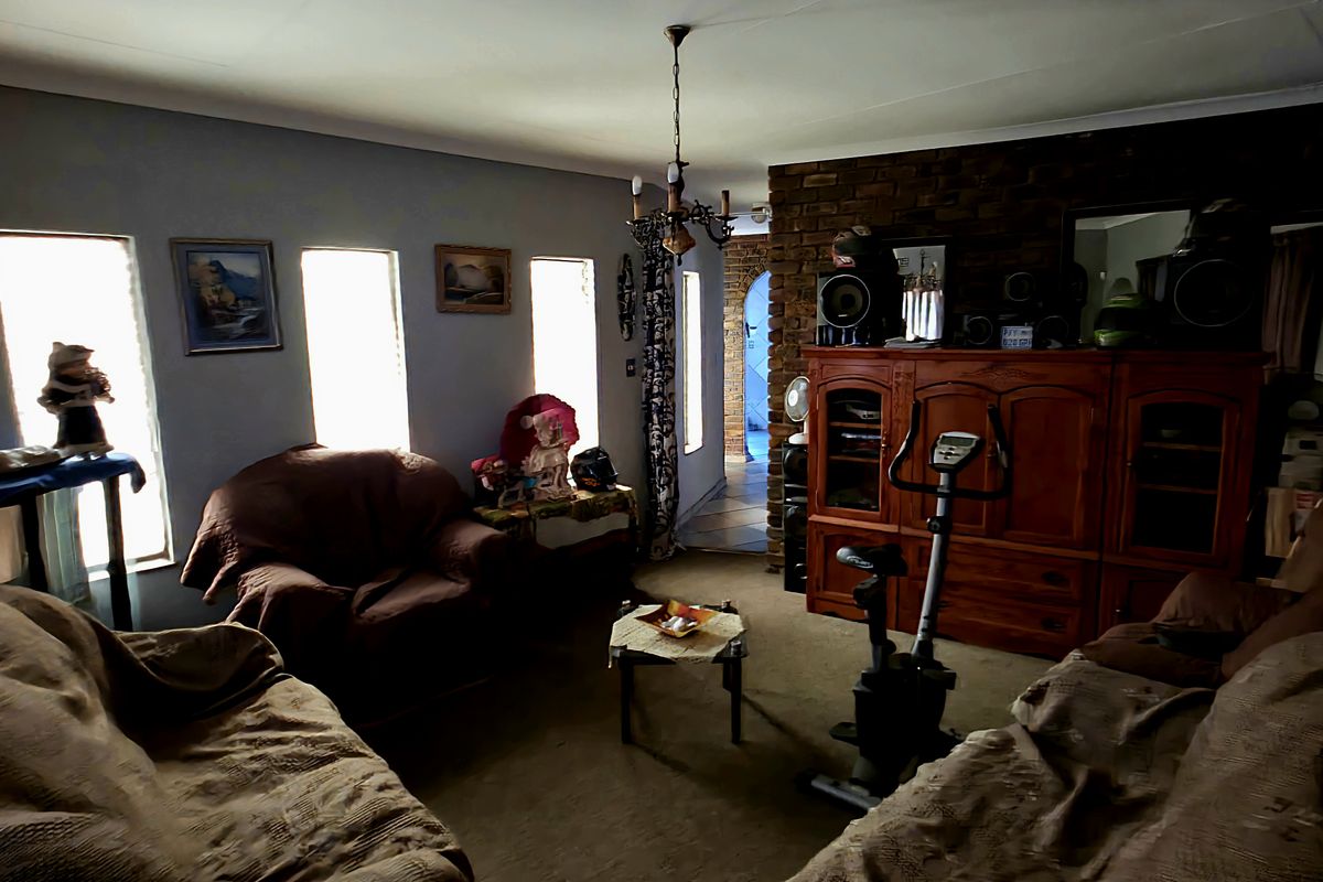 A living room featuring an exposed brick wall, coved ceilings, and a pendant light fixture, with carpeted flooring and access to an adjacent hallway.