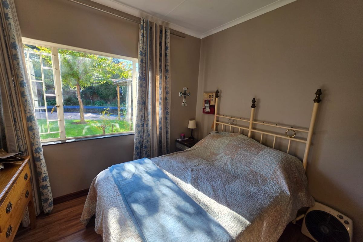 A cozy bedroom featuring laminate flooring, neutral wall tones, and a large window providing natural light and views of the garden.