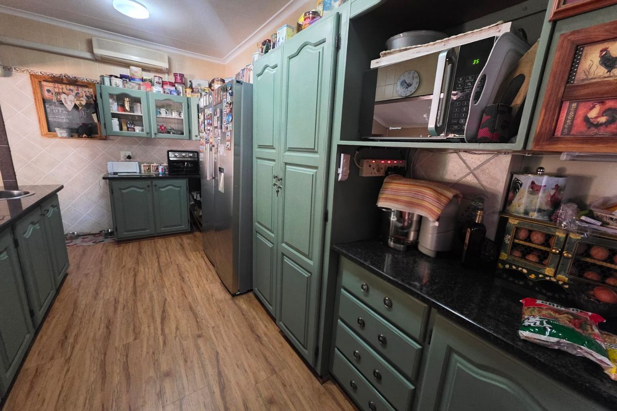 A functional kitchen featuring green painted cabinetry, dark granite countertops, laminate flooring, and a wall-mounted air conditioning unit.
