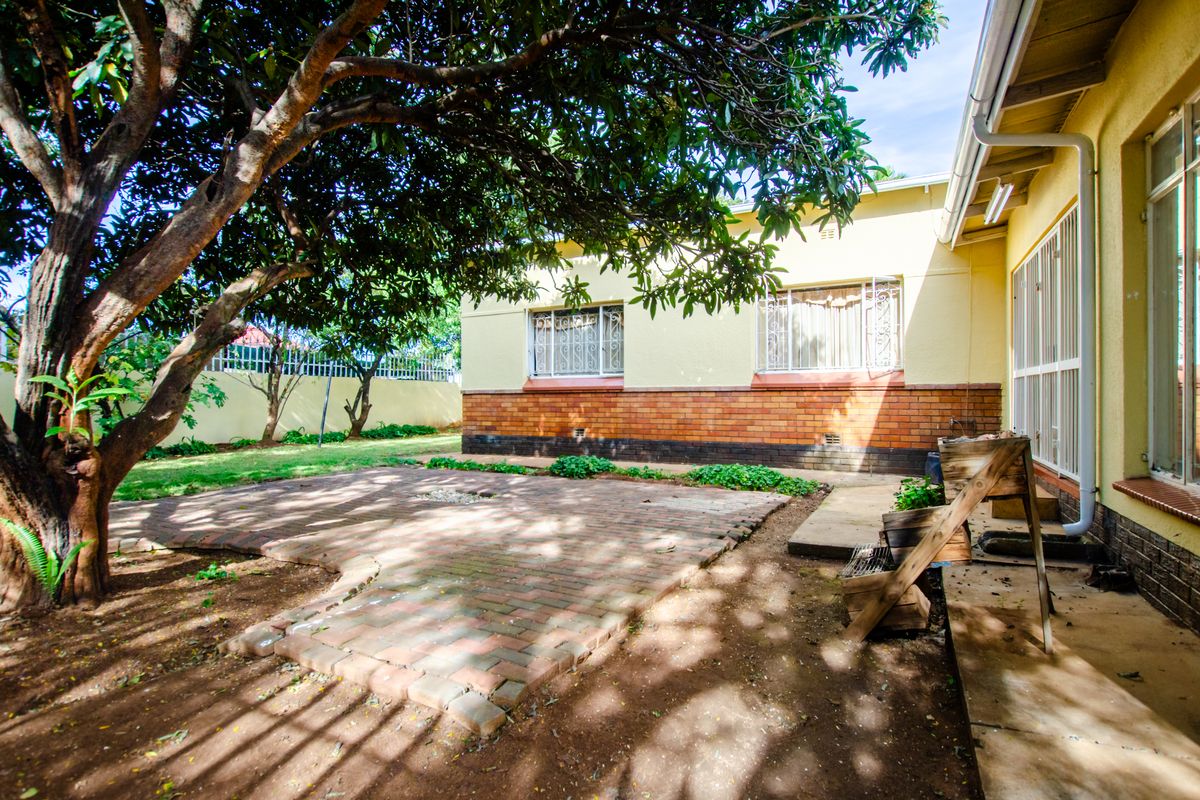 A rear garden area featuring a brick-paved patio, mature tree, and the rear elevation of the house with brick and plaster finishes.