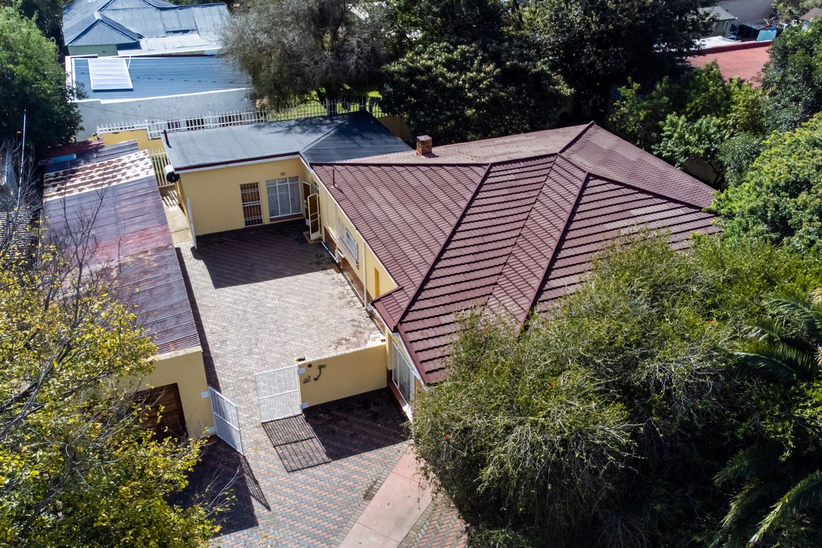 Aerial view of the property featuring a tiled main roof, paved courtyard area, and an adjacent outbuilding with corrugated metal roofing.