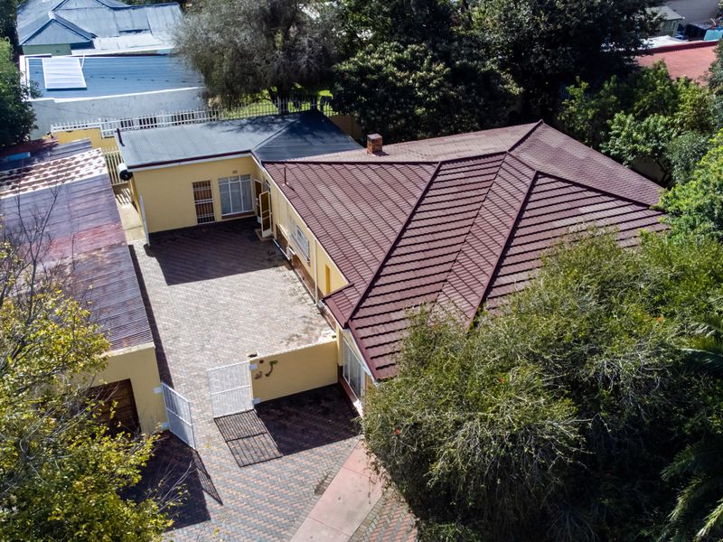 Aerial view of the property featuring a tiled main roof, paved courtyard area, and an adjacent outbuilding with corrugated metal roofing.