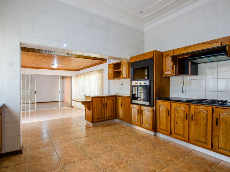 Spacious kitchen featuring wooden cabinetry, built-in oven, and hob, with an open-plan layout connecting to an adjacent living area.