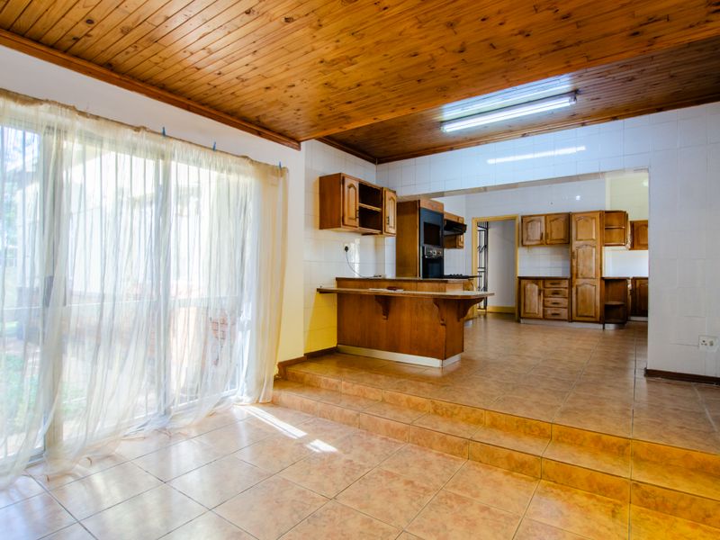 Open plan kitchen and living area featuring wooden cabinetry, tiled flooring, and a raised platform layout with direct access to the outdoor area.