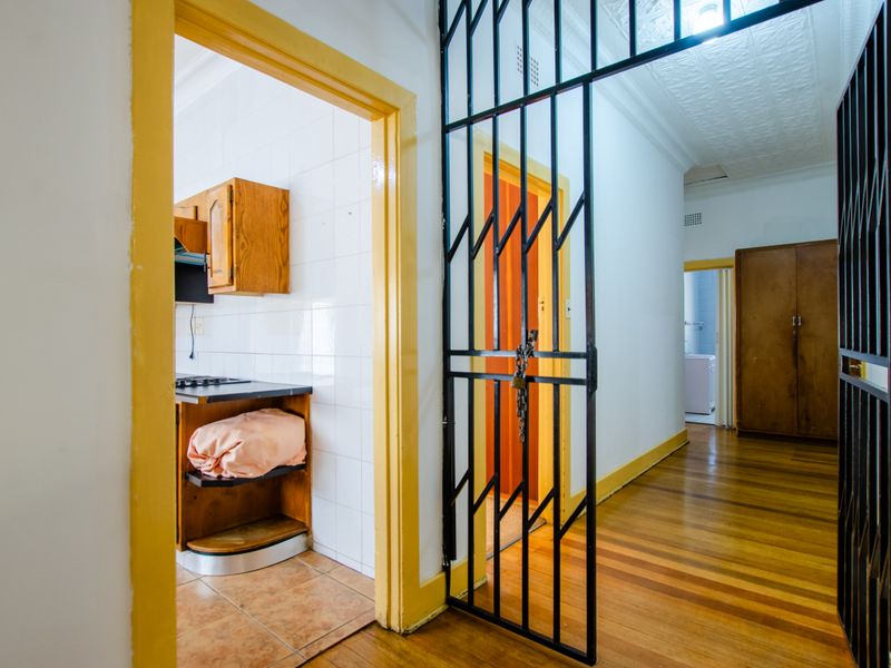 A view from the hallway looking into a kitchen area, featuring timber flooring, security gates, and traditional pressed metal ceilings.