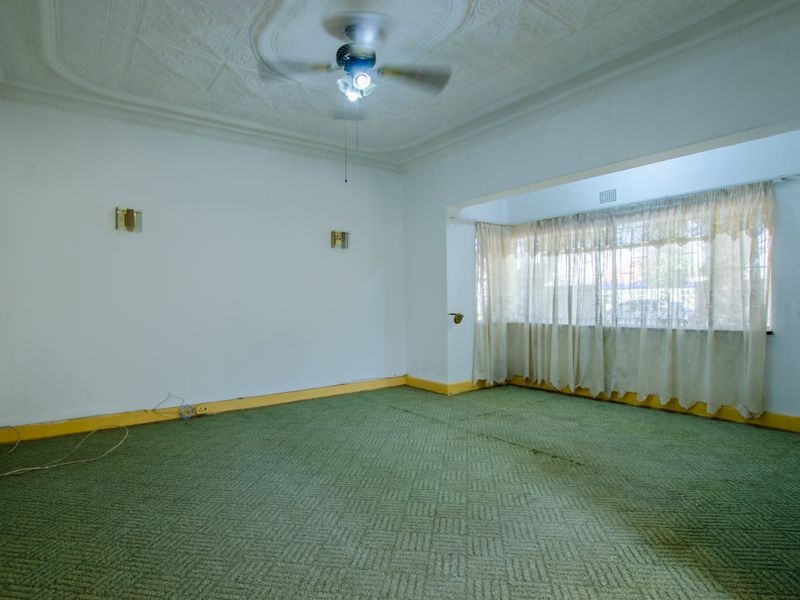 Spacious living room featuring a decorative pressed metal ceiling, ceiling fan, and large bay window with natural light.