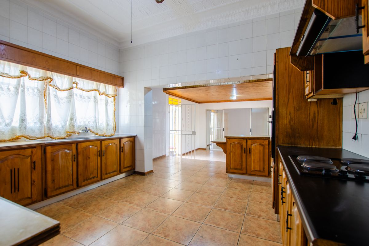 Spacious kitchen featuring traditional wooden cabinetry, tiled walls, and a built-in hob, offering a functional layout with an adjacent open-plan living area.