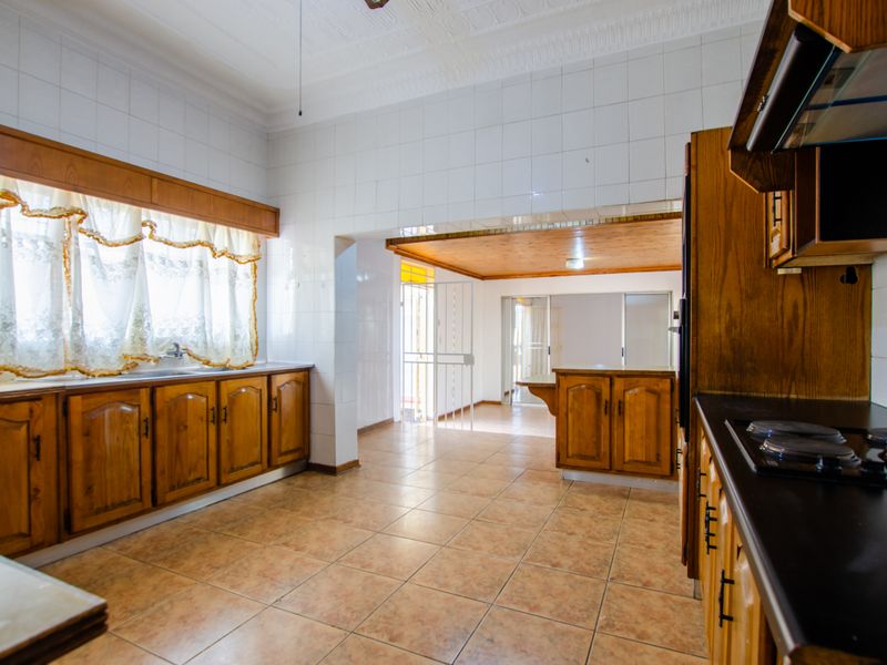 Spacious kitchen featuring traditional wooden cabinetry, tiled walls, and a built-in hob, offering a functional layout with an adjacent open-plan living area.