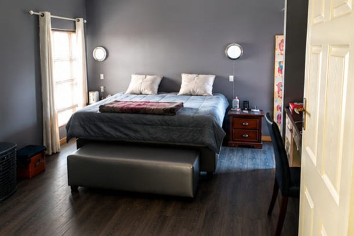 A well-maintained bedroom featuring dark laminate flooring, grey accent walls, and integrated wall-mounted lighting fixtures.