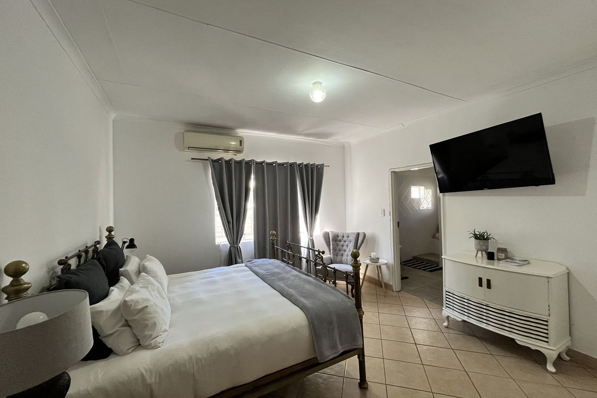 A bedroom featuring tiled flooring, a wall-mounted air conditioning unit, and an adjoining en-suite bathroom entrance.