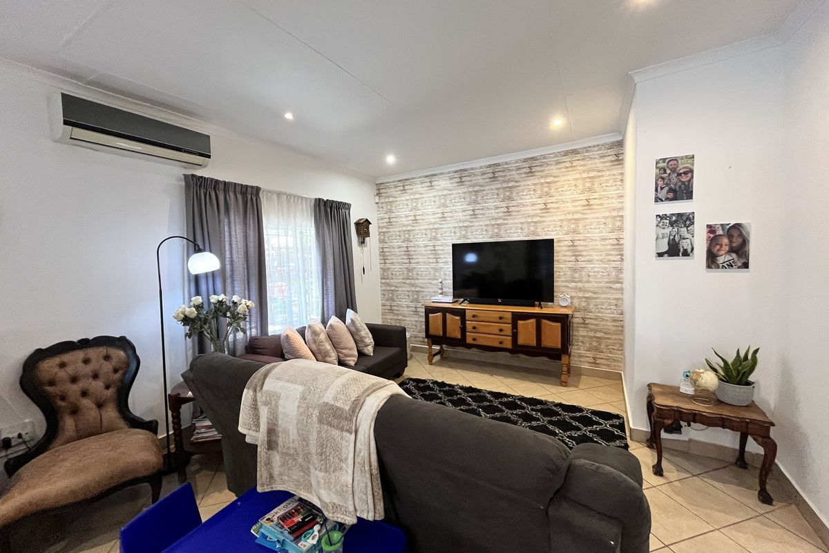 A comfortable living room featuring tiled flooring, a decorative wood-look feature wall, and a wall-mounted air conditioning unit.