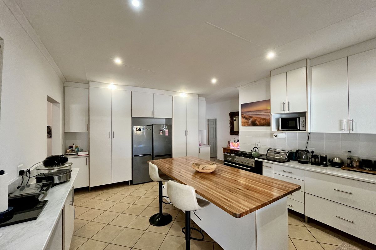 Modern kitchen featuring white cabinetry, a central island with a wooden countertop, tiled flooring, and built-in appliances including a gas stove and microwave.
